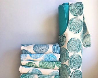 May include: A stack of 10 fabric squares with a blue and green circle pattern. The fabric squares are folded and stacked on top of each other. A blue and green fabric bag with a circle pattern is standing upright next to the stack of fabric squares.