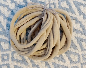 Puede incluir: Un primer plano de un paquete de cintas para el pelo de tela beige. Las cintas para el pelo están hechas de un material suave y elástico y son perfectas para sujetar el cabello.