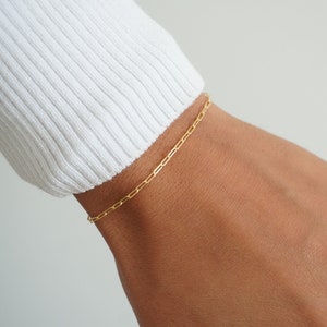 May include: A gold chain bracelet on a person's wrist.