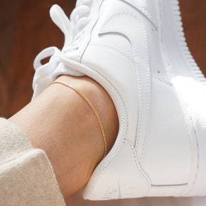 Peut inclure: Un bracelet de cheville en chaîne dorée sur la cheville d'une personne. Le bracelet de cheville est délicat et a un design simple.