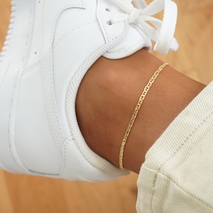 May include: A gold chain ankle bracelet on a person's ankle. The bracelet is a simple, delicate chain.