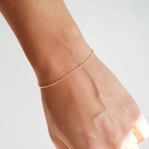 May include: A delicate gold chain bracelet on a person's wrist.