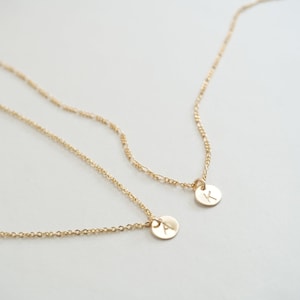 May include: Two gold necklaces with delicate chains and small round pendants. The pendants are engraved with the letters "A" and "K".