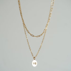 Peut inclure: Un collier à chaîne dorée à deux rangs avec un petit pendentif rond orné d'un motif de papillon.
