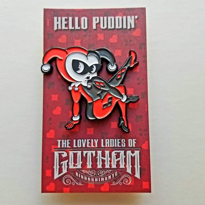 Puede incluir: Un pin de esmalte rojo y negro con Harley Quinn, un personaje de los c&oacute;mics de Batman. El pin representa a Harley Quinn en una pose juguetona con el texto "Hello Puddin'" y "The Lovely Ladies of Gotham" en la tarjeta.