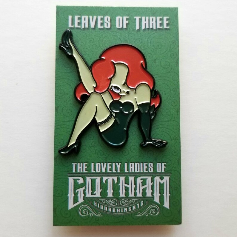 Puede incluir: Un pin de esmalte verde y blanco con una mujer de dibujos animados de pelo rojo, vestida con un atuendo verde y negro. El pin dice "Leaves of Three" y "The Lovely Ladies of Gotham" con una fuente estilizada.