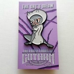 Puede incluir: Un pin de esmalte plateado con una representaci&oacute;n de dibujos animados de Catwoman, un personaje ficticio de los c&oacute;mics de Batman. El pin est&aacute; sobre un fondo morado con el texto "The Cat's Meow" y "The Lovely Ladies of Gotham" en una fuente de estilo vintage.