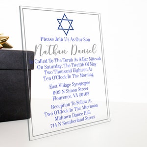May include: A clear acrylic invitation with a blue Star of David at the top. The invitation reads "Please Join Us As Our Son Nathan Daniel Is Called To The Torah As A Bar Mitzvah On Saturday, The Twelfth Of May Two Thousand Eighteen At Ten O'Clock In The Morning East Village Synagogue 609 N Simon Street Flourence, VA 20105 Reception To Follow At Two O'Clock In The Afternoon Midtown Dance Hall 714 N Southerland Street"