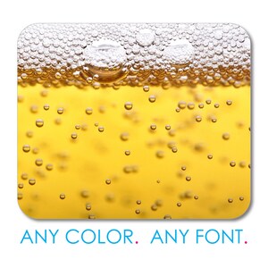 May include: Close-up of a glass of beer with a thick head of foam. The beer is a light golden color and there are many small bubbles throughout the liquid.