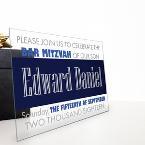 May include: A white and blue bar mitzvah invitation with the text "PLEASE JOIN US TO CELEBRATE THE BAR MITZVAH OF OUR SON Edward Daniel Saturday, THE FIFTEENTH OF SEPTEMBER TWO THOUSAND EIGHTEEN"