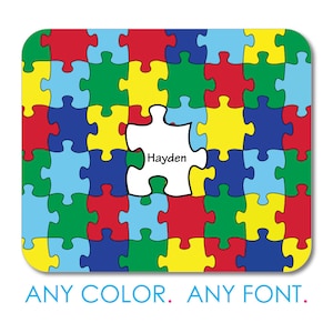 May include: A colorful puzzle-themed design with a white puzzle piece in the center, displaying the name "Hayden." The puzzle pieces are in various colors, including red, blue, yellow, and green. The text "ANY COLOR. ANY FONT." is at the bottom.