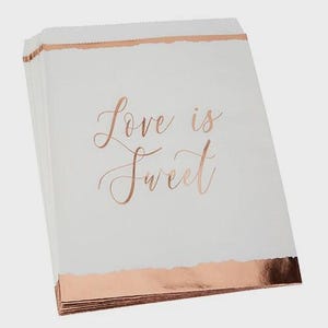 May include: A pile of white paper treat bags with rose gold detailing. The bags feature a torn edge design and the words "Love is Sweet" in elegant rose gold script. Suitable for weddings or celebrations.