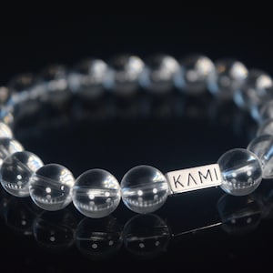 Könnte beinhalten: Ein Armband aus klaren Kristallperlen mit einem silbernen Anhänger, auf dem "KAMI" steht.