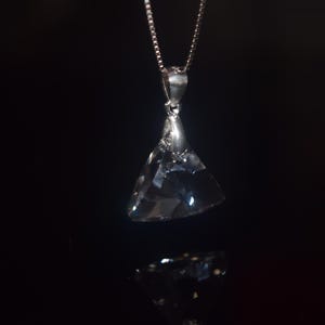 Könnte beinhalten: Eine silberne Kettenkette mit einem großen, klaren Kristallanhänger in Form eines Dreiecks.