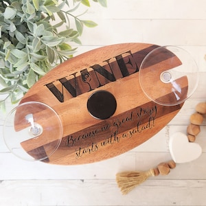 May include: Wooden serving tray with two wine glass holders. The tray is engraved with the word "WINE" and the text "Because no great story starts with a salad!"