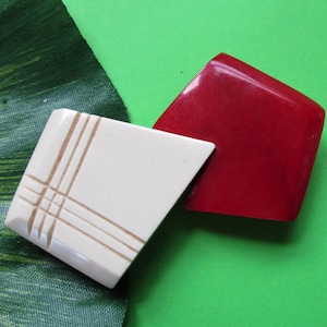 May include: A vintage brooch with two geometric shapes, one white with a crosshatch pattern and one red.