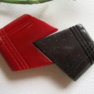 May include: A red and black geometric brooch made of plastic. The brooch is shaped like two overlapping triangles.