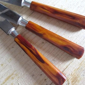 Könnte beinhalten: Drei vintage Küchenmesser mit braunen und orangefarbenen, marmorierten Kunststoffgriffen.