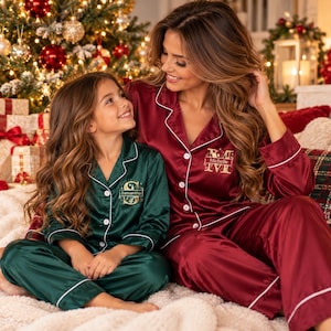 May include: Matching satin pajama sets featuring a button-down shirt and long pants with white piping. The dark green set is embroidered with the name Samantha and the letter S, while the burgundy set features the name Michelle and the letter M.