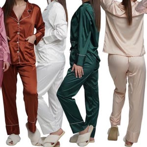 May include: A collection of satin pajama sets in various colors, including pink, brown, white, green, and beige. Each set features a button-down top with a notched collar and a matching pair of pants. The pajamas have white piping.
