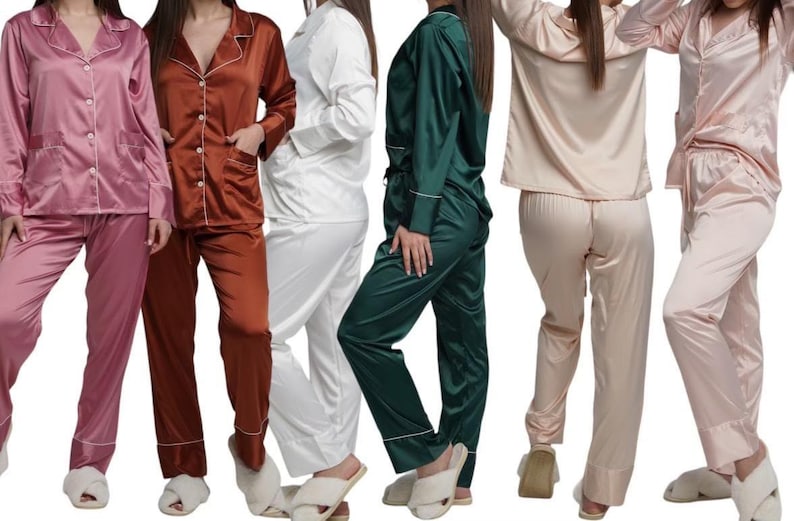 May include: A collection of satin pajama sets in various colors, including pink, brown, white, green, and beige. Each set features a button-down top with a notched collar and a matching pair of pants. The pajamas have white piping.