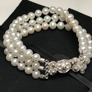 May include: A white pearl bracelet with a silver clasp. The bracelet is made of three strands of pearls.