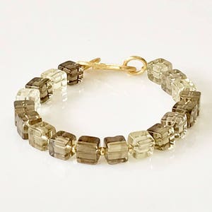 May include: A gold tone bracelet with a graduated ombre effect of clear and brown square beads.