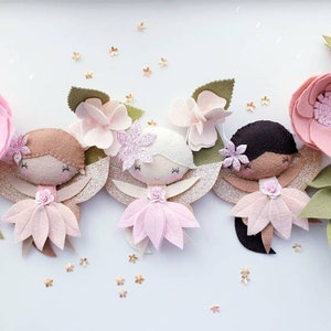 The garland features three pink felt fairies with glitter wings and different colour hair and skin tone. Each has a hand embroidered face and lightly blushed cheeks. On each side of the fairies are large pink felt flowers.
