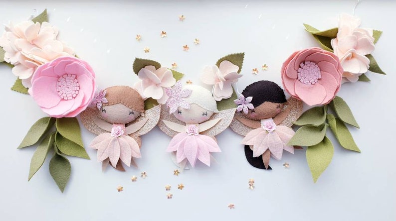 The garland features three pink felt fairies with glitter wings and different colour hair and skin tone. Each has a hand embroidered face and lightly blushed cheeks. On each side of the fairies are large pink felt flowers.