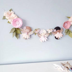 The garland features three pink felt fairies with glitter wings and different colour hair and skin tone. Each has a hand embroidered face and lightly blushed cheeks. On each side of the fairies are large pink felt flowers.