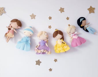 May include: A decorative garland featuring six felt dolls representing various characters in colorful dresses, interspersed with several gold glitter stars. The dolls have simple facial features and are suspended on a thin white string.