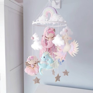 Op de afbeelding: Een witte houten babymobiel met een regenboog, wolken, een zeemeermin, een fee, een draak, een zeepaardje en gouden glittersterren.