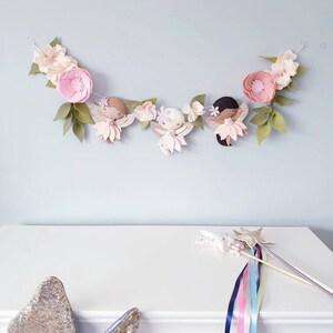 The garland features three pink felt fairies with glitter wings and different colour hair and skin tone. Each has a hand embroidered face and lightly blushed cheeks. On each side of the fairies are large pink felt flowers.