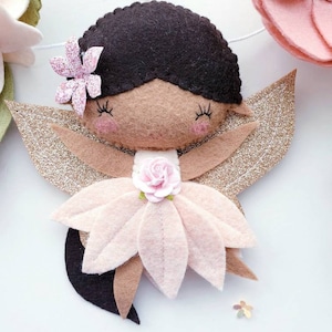 A felt fairy with brown hair, a pink flower dress, and gold glitter wings.