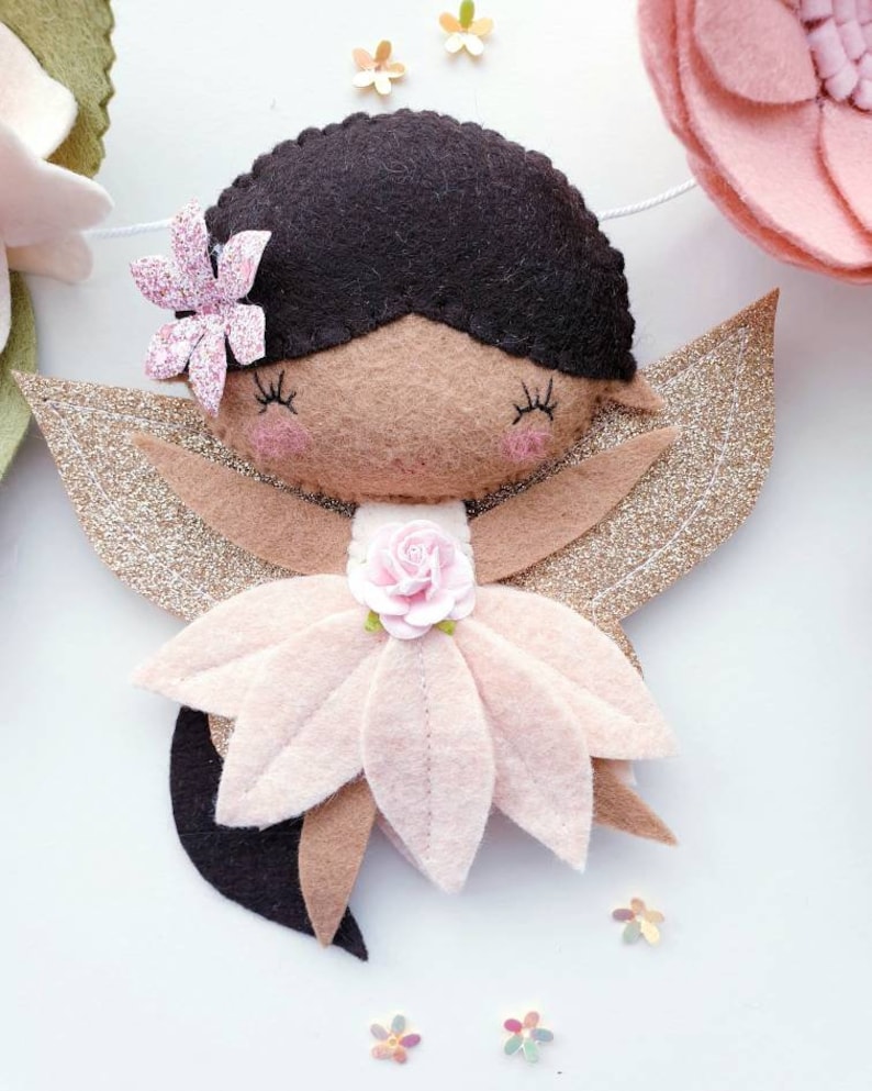 A felt fairy with brown hair, a pink flower dress, and gold glitter wings.