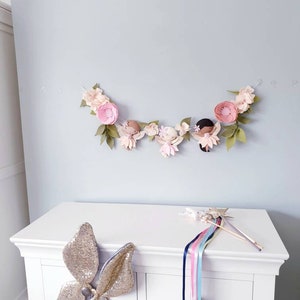 The garland features three pink felt fairies with glitter wings and different colour hair and skin tone. Each has a hand embroidered face and lightly blushed cheeks. On each side of the fairies are large pink felt flowers.