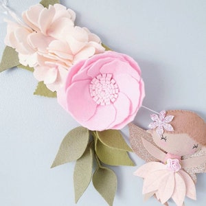 A felt garland with a pink flower, green leaves, and a pink fairy with glitter wings. The fairy has brown hair, a pink flower on her head, and a pink dress.