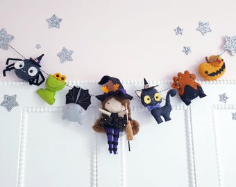 以下が含まれることがあります： ハロウィーンをテーマにしたフェルトガーランド。魔女の人形、黒猫、クモ、カエル、コウモリ、カボチャが特徴です。ガーランドは黒い糸でつながれ、キラキラ光る星のアクセントで飾られています。魔女の人形はほうきを持っています。