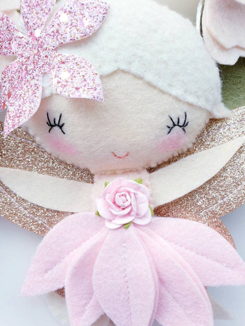 A pink felt fairy with gold glitter wings, a pink flower on her dress, and a pink glitter flower on her head.