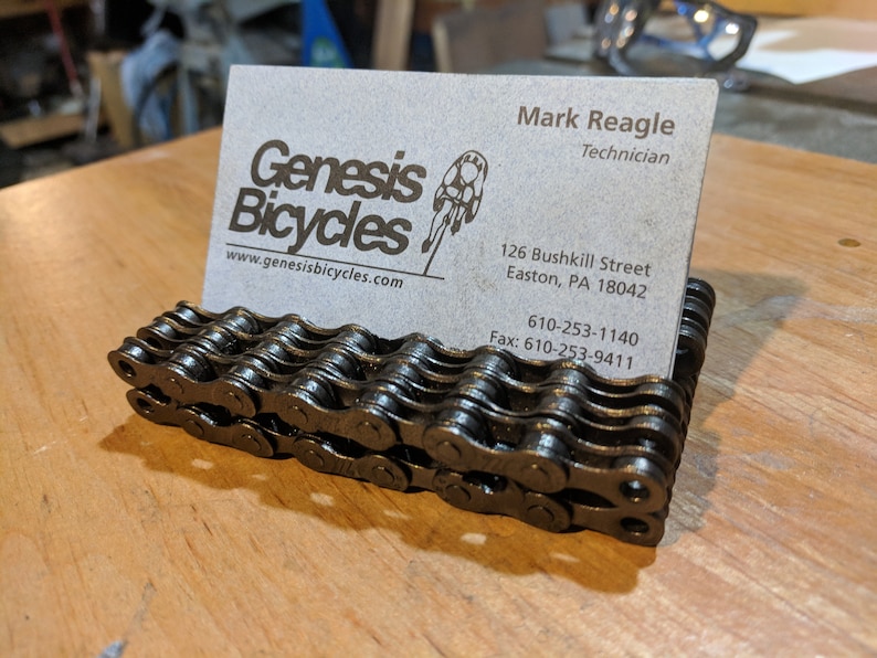 May include: A business card holder made of stacked bicycle chains. The business card is for Genesis Bicycles, a bicycle shop in Easton, Pennsylvania. The card includes the shop's website, address, phone number, and fax number.