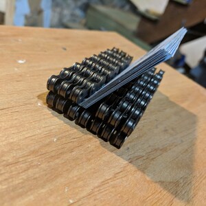 May include: A black metal business card holder made from a bicycle chain. The holder is filled with business cards.