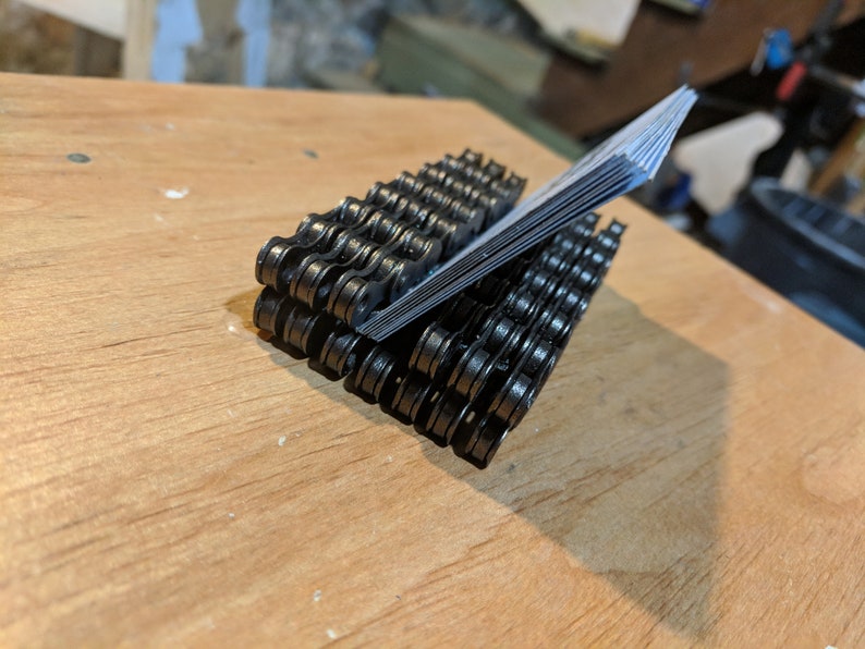 May include: A black metal business card holder made from a bicycle chain. The holder is filled with business cards.