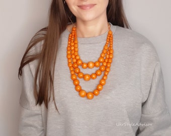Halsband med tre strängar av orange träpärlor, haklapp i flera lager, graderade varma, jordnära smycken i trä