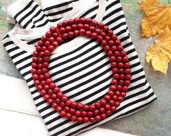 May include: A red wooden bead necklace on a striped black and white sweater. The necklace is made of multiple strands of beads.