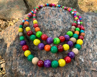May include: A multi-strand necklace made of colorful wooden beads. The beads are round and have a glossy finish. The necklace is layered and has a variety of colors, including red, orange, yellow, green, blue, purple, and brown.