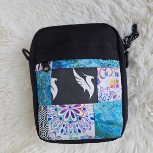 Puede incluir: Bolso bandolera negro con diseño patchwork. El patchwork presenta un cuadrado negro con un logotipo de pájaro blanco y cuadrados de tela estampada coloridos en azul, morado y blanco. El bolso tiene una correa negra ajustable y cierre de cremallera.