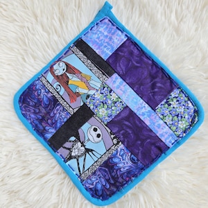 May include: A square quilted potholder featuring a patchwork design with purple, blue, and black fabric panels. The fabric displays printed illustrations of Jack Skellington and Sally from The Nightmare Before Christmas, alongside floral and abstract patterns.