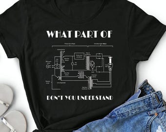 May include: A black short-sleeved t-shirt featuring a white graphic print of an X-ray circuit diagram. The text "WHAT PART OF" is printed above the diagram, and "DON'T YOU UNDERSTAND" is printed below the diagram in a bold, white sans-serif font.