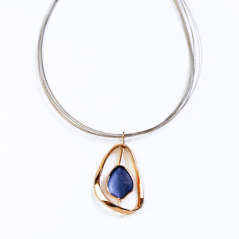 Adjustable Necklace with a brown steel wire chain and an open Pear shape rose gold pendant with a floating textured disc center painted in blue enamel on a white background