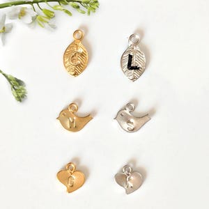 May include: Six different charms with letters on them. There are two gold leaf charms with the letters C and G, two silver leaf charms with the letters L and K, a gold bird charm with the letter M, and a silver bird charm with the letter S.
